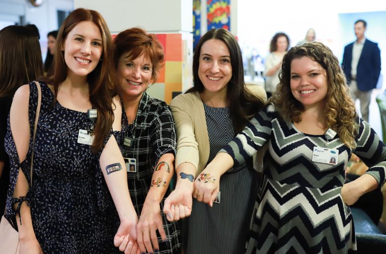Four women with their arms outstretched show their temporary tattoos. 