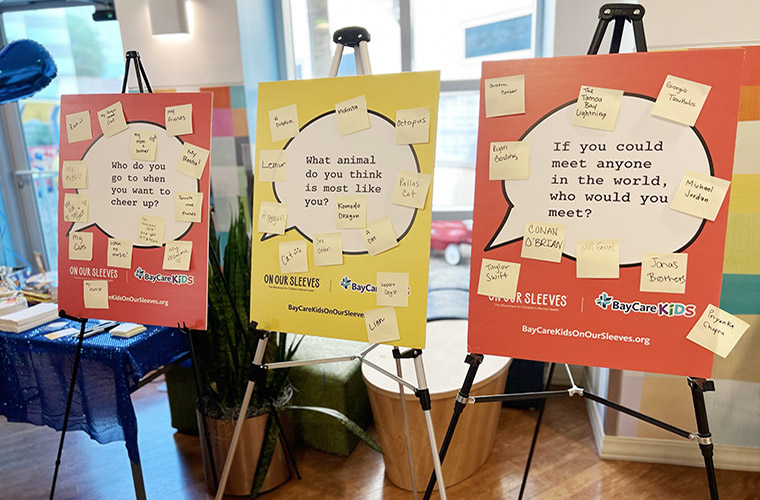 Three posterboard signs on easels are displayed with questions on them answered on yellow sticky notes. 