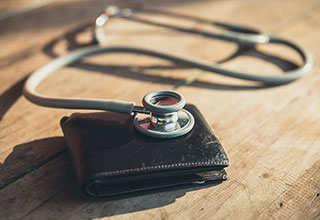 A silver stethoscope rests on top of a black wallet 