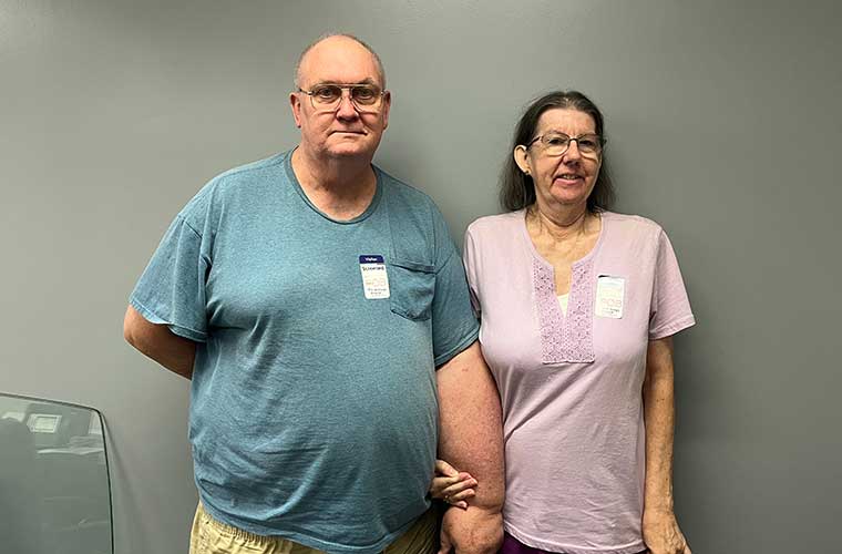 Kurt McDuffie, with his wife Joanne, suffers from lymphedema in his left arm caused by the removal of his breast due to cancer in 2015. He is wearing a blue shirt and she is wearing a pink shirt.