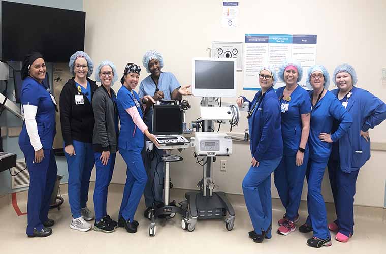 A group of nurses and technicians pose around a surgical robot.