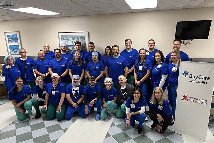 27 medical staff kneeling and standing in front of stand-up banner that reads "BayCare Orthopedics Operation Walk USA."