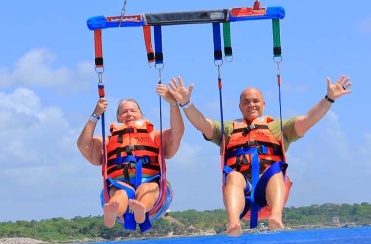 Kathleen is on the left parasailing on a body of water with her son Timothy on the right. Both are in harnesses.  