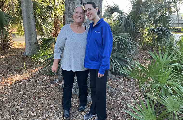 Kathleen Lillie (left) with health coach Courtney St. Louis (right) smiling and standing together outside among trees in a nature area. 