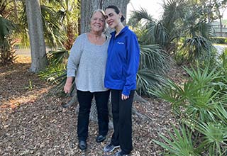 Kathleen Lillie (left) with health coach Courtney St. Louis (right) smiling and standing together outside among trees in a nature area. 