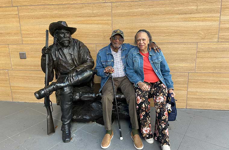An older couple sit on a bench next to a statue outside a museum.