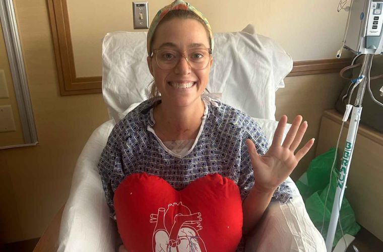 Brittany sits in a chair in her hospital gown at the hospital smiling and holding a stuffed heart.