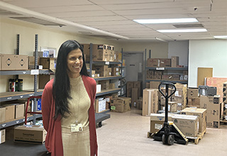 Woman with long dark hair stands in a room surrounded with boxes.