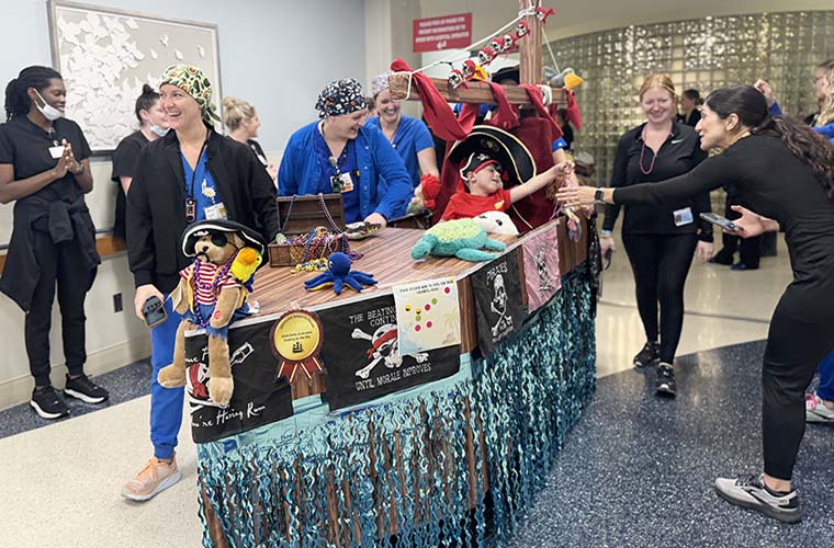 A young boy rides on a float and hands out beads to nurses in a hospital hallway.