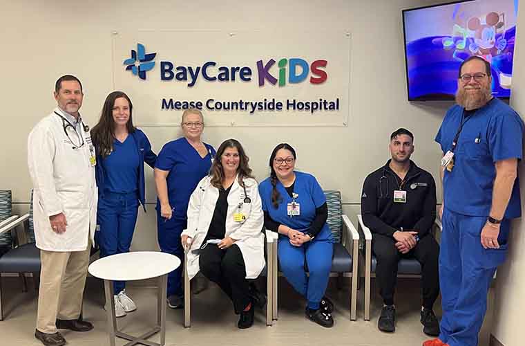 A diverse group of  specially trained pediatric nurses and physicians wearing scrubs stand  together in the Mease Countryside Hospital Pediatric Emergency Room.