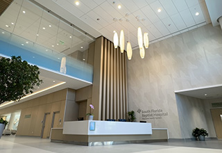 An elegant hospital lobby, with high vaulted ceilings and grouping of pendant lights suspended over the welcome desk.