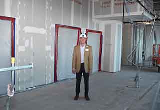 St. Joseph’s Hospital-South president Patrick Downes wearing a hard hat in front of unfinished walls and a spot where elevators will be. 