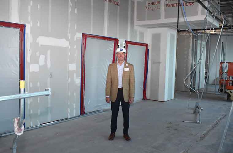 St. Joseph’s Hospital-South president Patrick Downes wearing a hard hat in front of unfinished walls and a spot where elevators will be.  