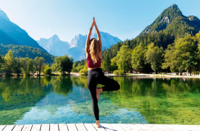 A woman practicing yoga on a dock by a serene lake.