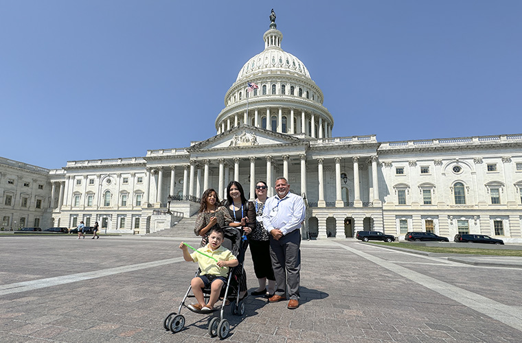 A young girl, two women and a man stand behind a boy in a stroller. They are in front of the U.S. Capitol building.