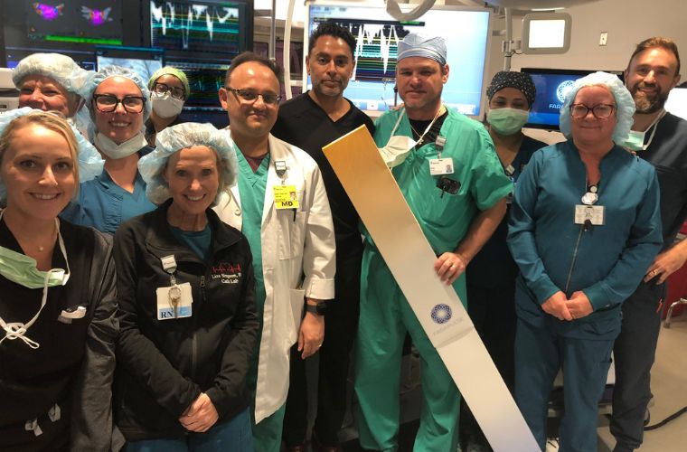 The surgical team stands in an operating room with monitors behind them.
