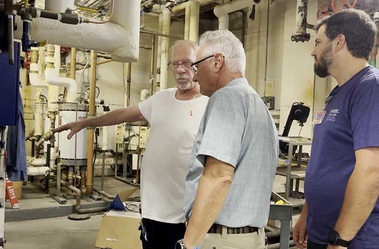 Three men talk in a room that is filled with large equipment. 