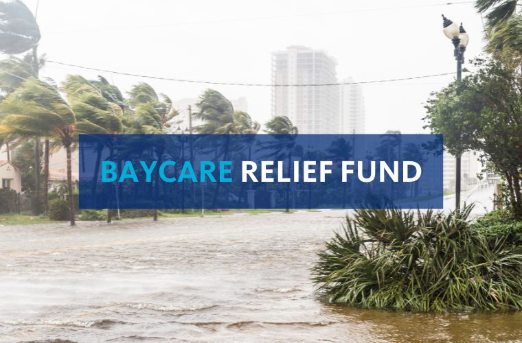 Visual representation of the BayCare Relief Fund, highlighting its mission to provide aid and resources to individuals in crisis. The image in the background shows a hurricane scene of a city skyline and palm trees blowing in the wind with the text BayCare Relief Fund in all caps in a blue text box in front. BayCare is in light blue, and Relief Fund is in white.