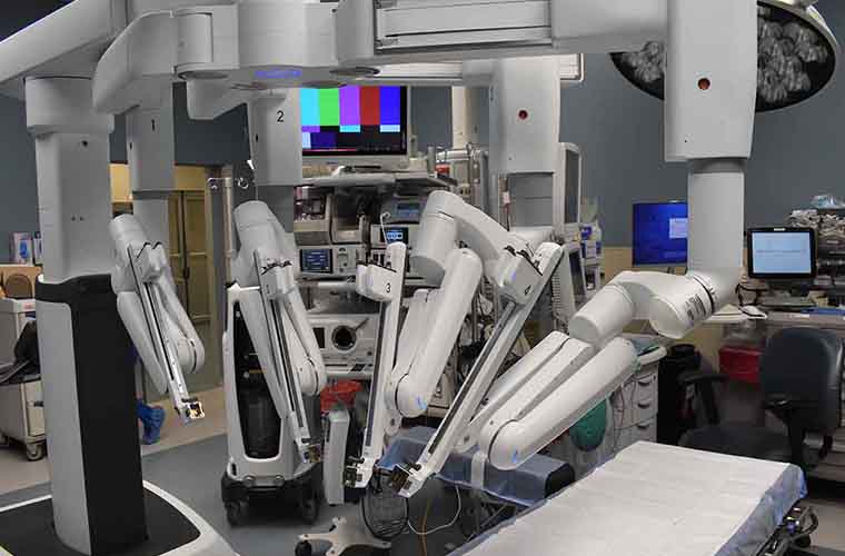 A modern operating room equipped with a da Vinci surgical system, featuring multiple robotic arms and a patient table, surrounded by various medical monitors and equipment.