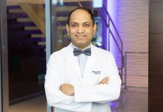 Dr. Subhasis Misra, pictured in a smiling headshot, dons a white lab coat over a blue button-down shirt complemented by a stylish bow tie.