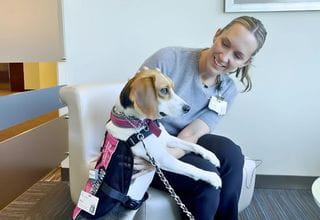  A woman in a chair with a therapy dog on a leash, enjoying a moment together.