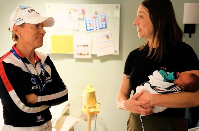 A female golf professional speaks with a mother holding her small newborn inside a NICU room at Morton Plant Hospital.