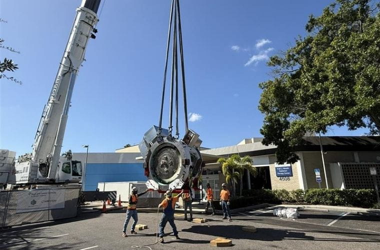 A large crane lifts the proton therapy accelerator as construction workers guide it into place outside St. Joseph’s Hospital in Tampa.