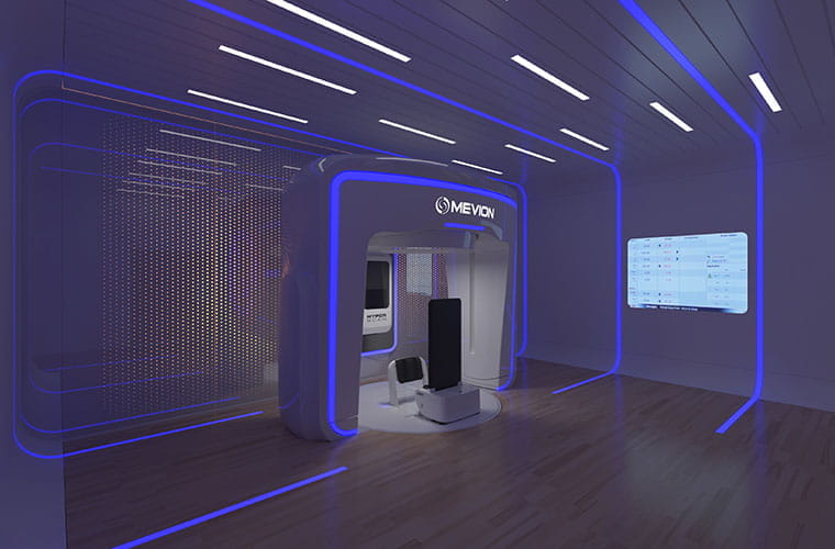The new proton therapy system in an open room. There is an upright area meant for patients to stand in while surrounded by the open large square. There are blue lights that accent the equipment.