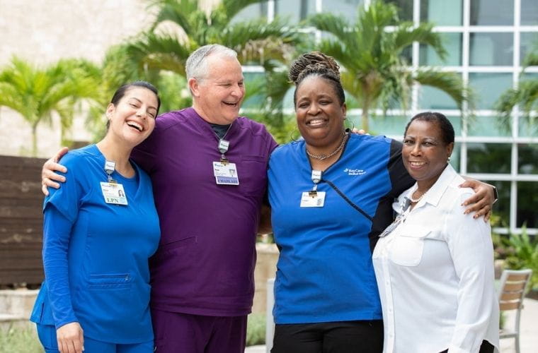 BayCare team members wearing clinical and professional attire stand together outdoors on a hospital campus.