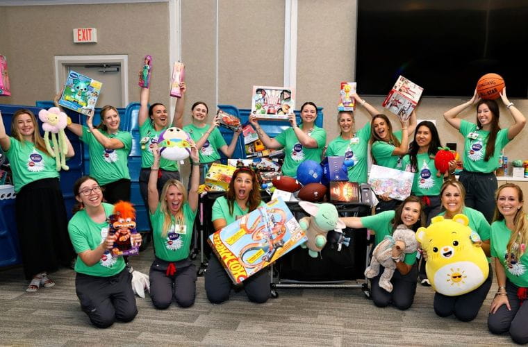 A group of BayCare team members wearing green Christmas in July shirts pose around carts filled with donated toys, stuffed animals, games and sports equipment collected for pediatric patients at BayCare's St. Joseph's Children's Hospital. 
