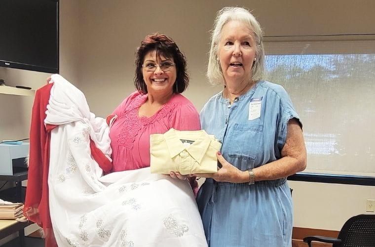 Two women hold handmade infant remembrance garments, including a white gown with silver embellishments and a coordinated outfit, at BayCare's Winter Haven Women's Hospital.