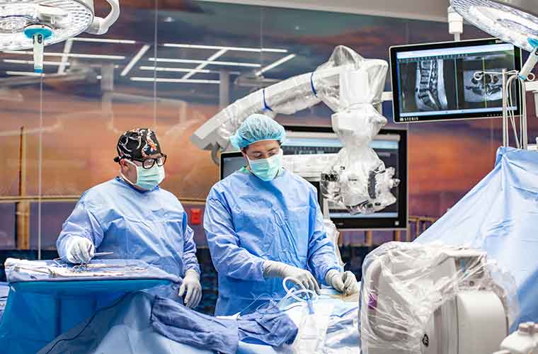 Two men dressed is surgical scrubs stand at a surgical table in an operating room.