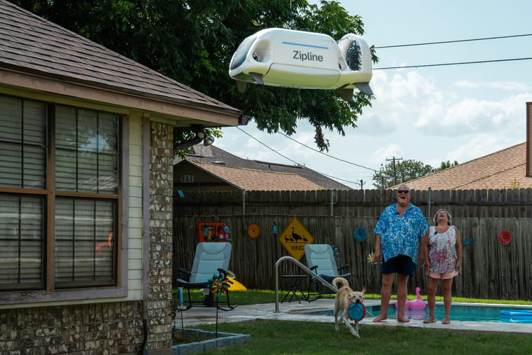 A Zipline delivery drone delivers a package to a couple in their backyard.