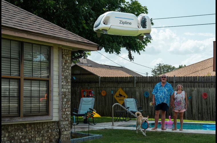 A Zipline delivery drone delivers a package to a couple in their backyard.