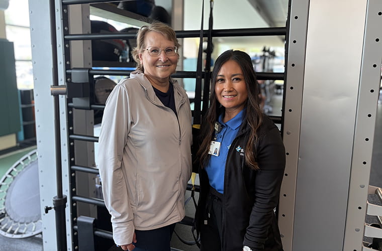 Two women standing in front of gym equipment, one wearing athletic clothing and the other in a BayCare uniform. 