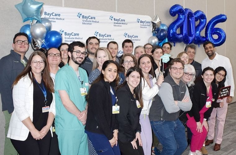 Group of BayCare Graduate Medical Education residents and staff pose together in front of a BayCare-branded backdrop, decorated with blue and silver balloons and large “2026” number balloons, celebrating Match Day.