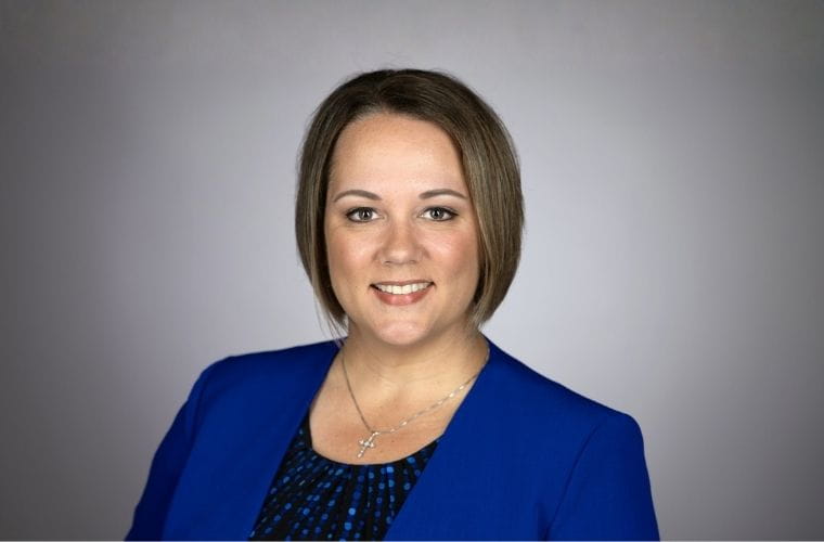 Portrait photo of a woman with short brown hair, wearing a black blouse with blue circular designs and a blue jacket.