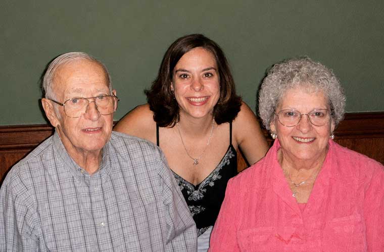 A young woman stands between to older people as those pose for a picture in a restaurant. 