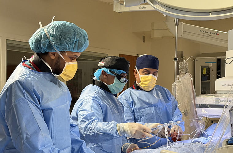 Three people in surgical scrubs and masks in a surgical suite who appear to operating on a patient.