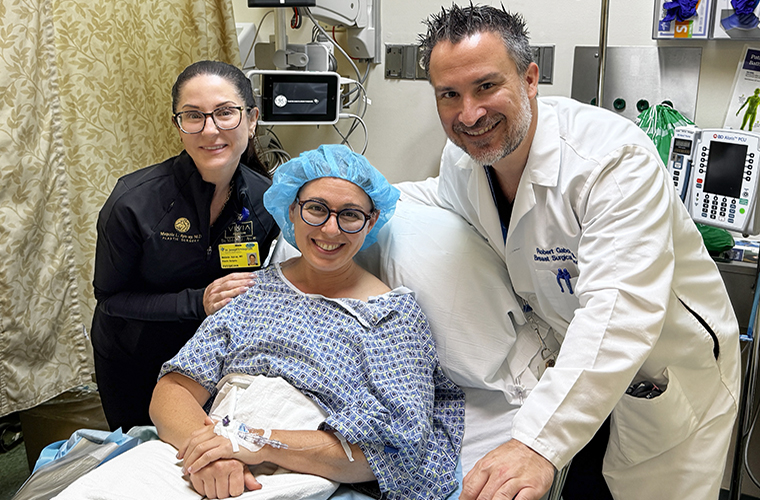 Hospital room scene with a smiling patient in a hospital gown on a bed, surrounded by two doctors. Medical equipment visible in the background. 