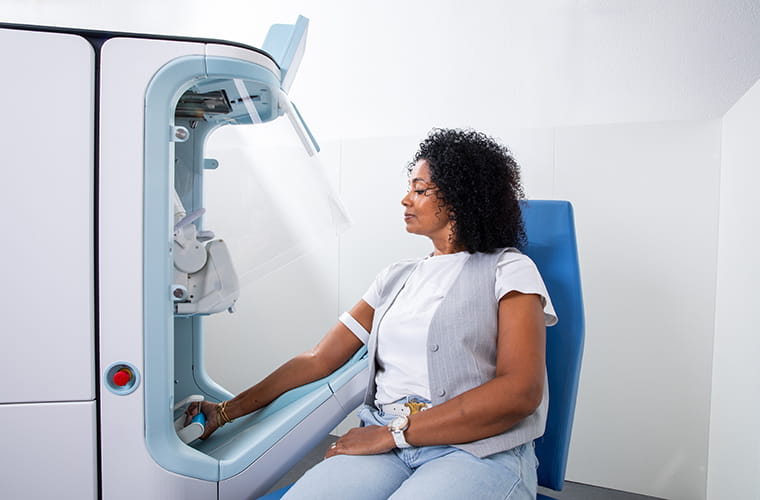 Person seated beside an Aletta robotic blood-draw device with one arm resting in its arm support.
