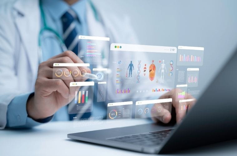 A person in a white medical coat uses a laptop while interacting with digital healthcare dashboards displaying charts, patient data and medical illustrations on a transparent virtual interface.
