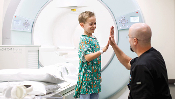 radiology technician high fiving a small boy in front of an MRI machine