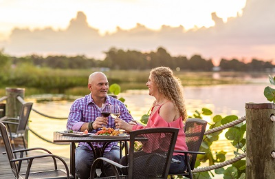 A couple is having dinner at a table outside next to a lake.