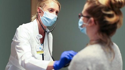 A physician examines a patient, and both are wearing masks.