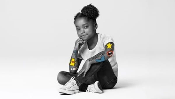 A young girl sitting on the floor with her arms crossed, participating in the "On Our Sleeves" campaign for mental health awareness.