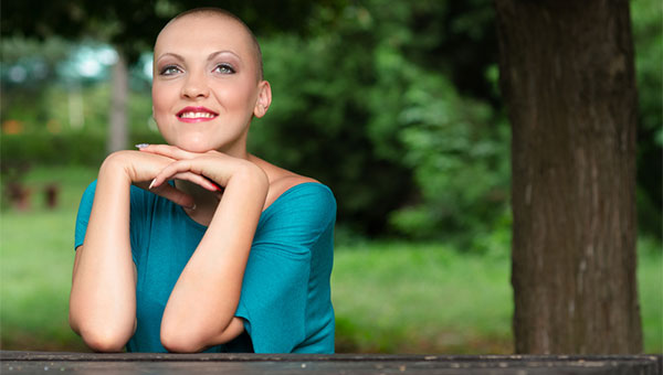 A smiling female cancer survivor is sitting outside under a tree.