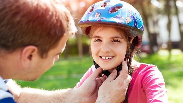 A father is adjusting the chin strap on his daughter's bicycle helmet.
