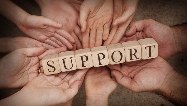 Hands are holding up wood blocks that spell the word "support."