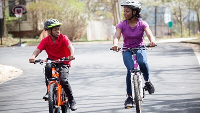 A brother and sister are wearing helmets while riding their bicycles in their neighborhood.